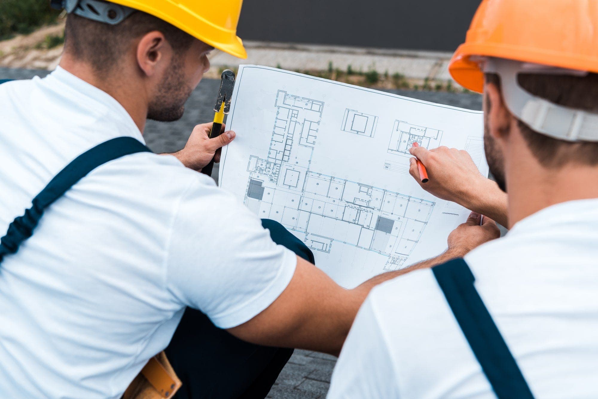 Two professional contractors in overalls and hardhats analyze a home blueprint for their project.